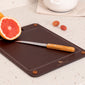 Brown slim cutting board with a knife and sliced grapefruit on a light surface